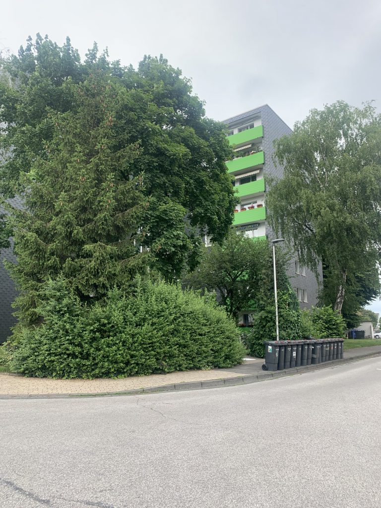 Bäume und Hecken vor Wohnhaus mit grünen Balkonen