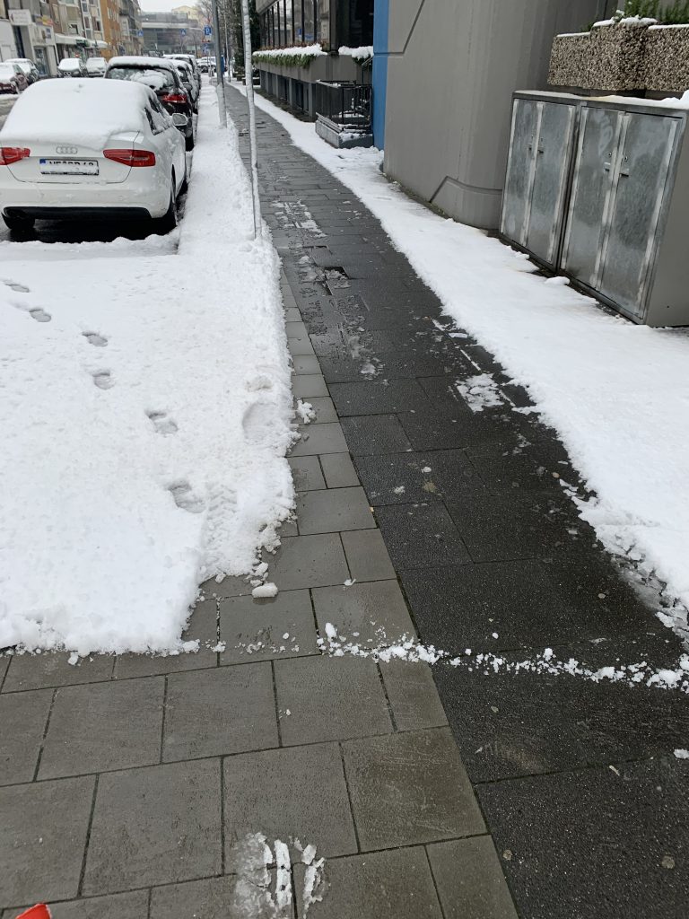 Öffentlicher Gehweg nach Winterdienst in Düsseldorf und parkendes Auto im Schnee