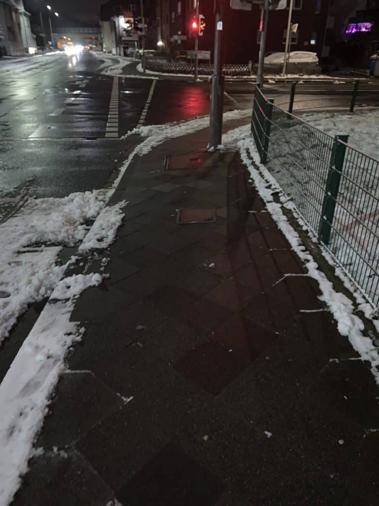 Gehweg zwischen Straße und Zaun bei Nacht im Winter