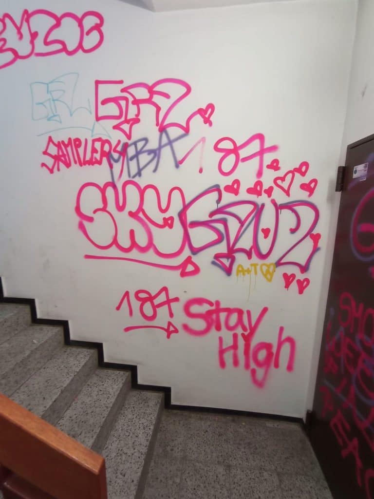 Pinke Graffitis auf weißer Wand über einer Treppe